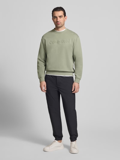 Männermodel trägt Sweatshirt mit Rundhalsausschnitt und Logo von CK Calvin Klein, Baumwoll-Elasthan-Mix, Regular-Fit, Ganzkörperansicht von vorne.