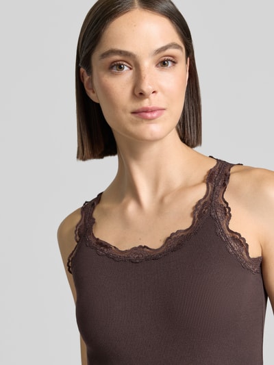 Frauenmodel trägt Slim Fit Top aus reiner Baumwolle mit Spitzenbesatz von Rich & Royal in Braun, Rundhalsausschnitt, Nahaufnahme Oberkörper.