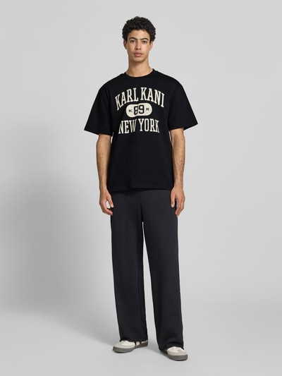 Männermodel trägt Oversized Fit Herren T-Shirt mit Logo-Print Modell 'Heritage' von KARL KANI in Schwarz, Reine Baumwolle, Rundhalsausschnitt, Rückenlänge bei Größe M 71 cm, Ganzkörperansicht von vorne.