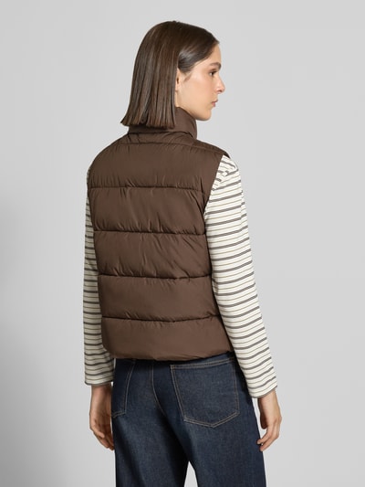 Frauenmodel trägt Regular Fit Weste in Stepp-Optik von camel active in Braun, gestreiftes Shirt, Jeans, Ganzkörperansicht Rückansicht. Damen Weste von camel active, Stepp-Optik, Regular Fit, Stehkragen, Zweiwege-Reißverschluss, Eingrifftaschen, Rückenlänge bei Größe 36: 55 cm, Schulterbreite bei Größe 36: 39 cm, Brustweite bei Größe 36: 52 cm.