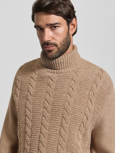 Mannmodel draagt Pullover aus Wolle mit Rollkragen van Barbour, structuur breisel met kabelpatroon, effen beige kleur, close-up bovenlichaam.