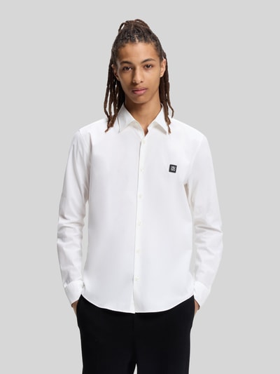 Männermodel trägt Slim Fit Freizeithemd aus Baumwoll-Mix Modell 'ERMO' von HUGO, weiß, Kentkragen, Label Patch, Ganzkörperansicht von vorne.