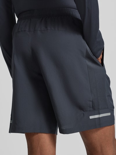 Männermodel trägt Tech Utility Shorts mit Label-Print von Under Armour, prosty krój, elastyczny pas, styl utility, nadruk z logo, szerokość w rozmiarze M 37 cm, długość wewnętrzna nogawki w rozmiarze M 22 cm, całkowity widok z tyłu