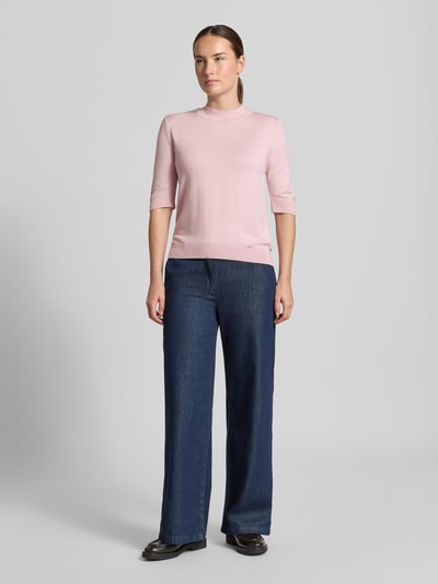 Frauenmodel trägt Strickpullover aus Viskose-Mix von MORE & MORE in Rosa mit Stehkragen, taillierte Passform, Ganzkörperansicht von vorne.