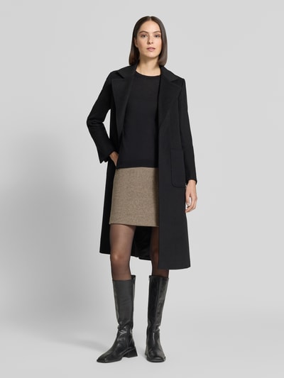 Frauenmodel trägt Minirock mit elastischem Bund Modell 'WOLCA' von ICHI in Beige mit Struktur-Muster, kombiniert zu schwarzem Mantel, Ganzkörperansicht von vorne.