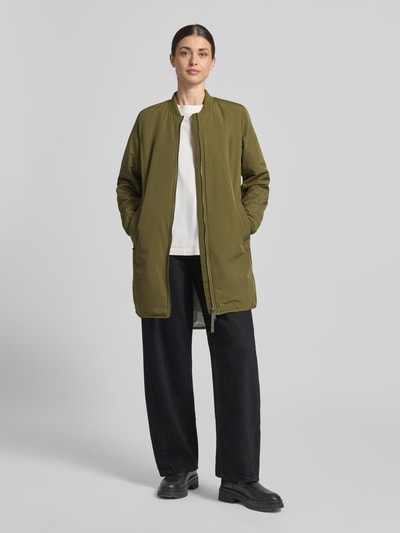 Frauenmodel trägt Jacke mit Zweiwege-Reißverschluss von camel active in Oliv, Lockerer-Schnitt, Stehkragen, extralang, Ganzkörperansicht von vorne. Rückenlänge 92 cm, Schulterbreite 42 cm, Brustweite 55 cm, Ärmellänge 64 cm, elastische Ärmelabschlüsse.