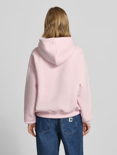 Frauenmodel trägt Regular Fit Hoodie mit Känguru-Tasche Modell 'Iconic' von Gina Tricot aus Baumwoll-Mix, zartrosa Farbe, elastische Abschlüsse, Ganzkörperansicht Rückansicht.