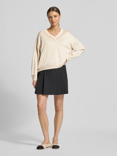 Frauenmodel trägt Relaxed Fit Pullover aus Viskose-Mix in Strick-Optik von LIU JO SPORT mit semitransparenten Partien, V-Ausschnitt, elastischen Abschlüssen, langärmelig, cremefarben zu schwarzem Rock, Ganzkörperansicht von vorne.