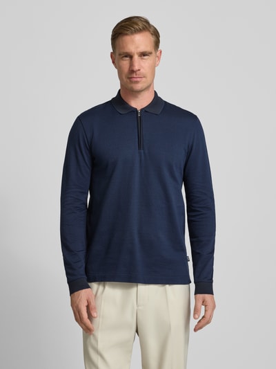 Męski model nosi Regular Fit Poloshirt aus reiner Baumwolle Modell 'PEDUZZI 06' od BOSS, granatowy kolor, wzór allover, widok z przodu, zdjęcie całej sylwetki. Materiał merceryzowany, długi rękaw z prążkowanym mankietem, polo kołnierzyk, rozcięcia po bokach, kontekst: męska koszulka polo z czystej bawełny.