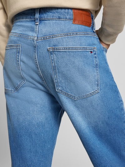 Männermodel trägt Tapered Fit Jeans aus Baumwoll-Mix von Tommy Jeans in Denim-Optik mit Label Patch, 5-Pocket-Design, Ganzkörperansicht Rückansicht