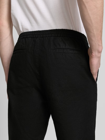 Mężczyzna nosi Leinenhose mit elastischem Bund und Eingrifftaschen od GAP, czarny kolor, mieszanka lnu i bawełny, krój loose fit, widok z tyłu, detal tylnych kieszeni, zbliżenie na górną część spodni.