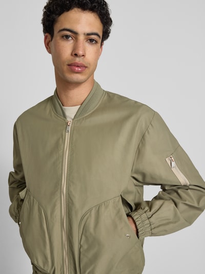 Männermodel trägt Bomberjacke mit Reißverschlusstasche am Ärmel von Replay in Khaki, Baumwoll-Mix, Gerader-Schnitt, Nahaufnahme Oberkörper.