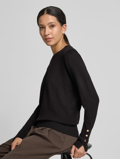 Vrouwenmodel draagt gebreide pullover van viscosemix met knopen aan de mouwboorden Model 'KATIE' van FREE/QUENT, recht model, ruglengte bij maat S 58 cm, mouwlengte 66 cm, bruine broek, volledige zijaanzicht