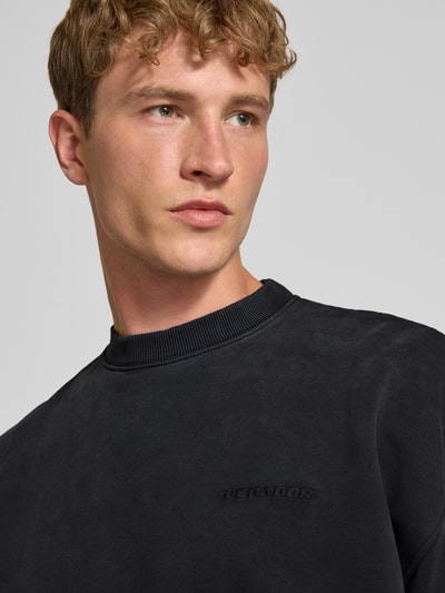 Männermodel trägt Relaxed Fit Sweatshirt aus Baumwoll-Mix von PEGADOR in Schwarz, Logo-Stickerei, glatte Textur, Nahaufnahme Oberkörper.