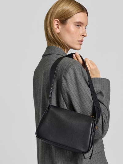 Frauenmodel trägt Shoulder Bag mit Strukturmuster von Tory Burch in Schwarz, rechteckige Form, strukturierte Lederoptik, Nahaufnahme Oberkörper. Hauptfach mit Reißverschluss, verstellbarer Schulterriemen, Steckfach mit Knopf, Maße ca. 43x17x9 cm.