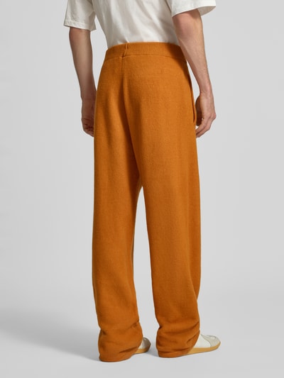 Männermodel trägt Wide Leg Weite Hose mit Woll-Anteil von adidas Originals in Orange; lockere Passform, glatte Textur, Ganzkörperansicht Rückansicht.