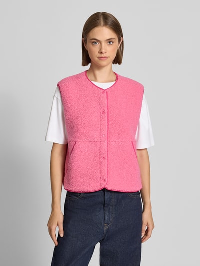 Kobiece modelka nosi Regular Fit kamizelkę z futerka Model 'Vera' od JJXX, różowy kolor, wpuszczane kieszenie, okrągły dekolt, bez rękawów, listwa guzikowa, długość tyłu w rozmiarze S: 54 cm, szerokość ramion w rozmiarze S: 43 cm, szerokość w klatce piersiowej w rozmiarze S: 50 cm. Widok całej sylwetki z przodu.