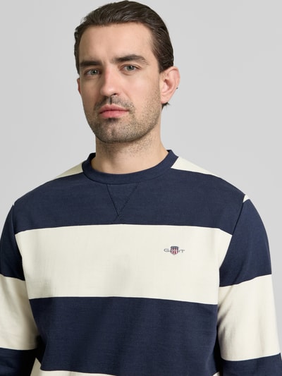 Männermodel trägt Regular Fit Pullover in Strick-Optik von Gant, navy-beige Streifen, Baumwolle, Logo-Stitching, Nahaufnahme Oberkörper.