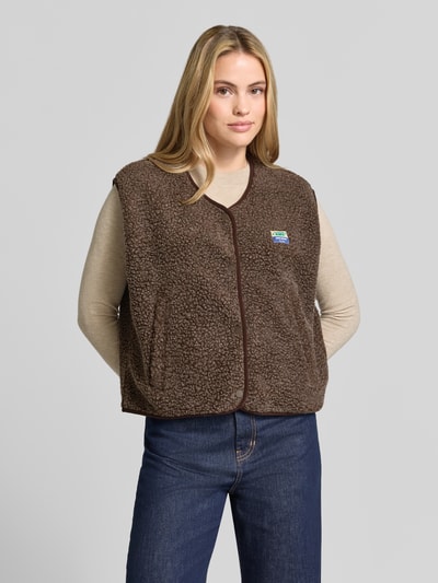 Frauenmodel trägt Relaxed Fit Weste aus Teddyfell Modell 'Hoktown' von American Vintage, braun, Logo-Patch, Ganzkörperansicht von vorne. Damen Weste aus Teddyfell, Knopfleiste, Rückenlänge 56 cm, Schulterbreite 43 cm, Brustweite 63 cm.