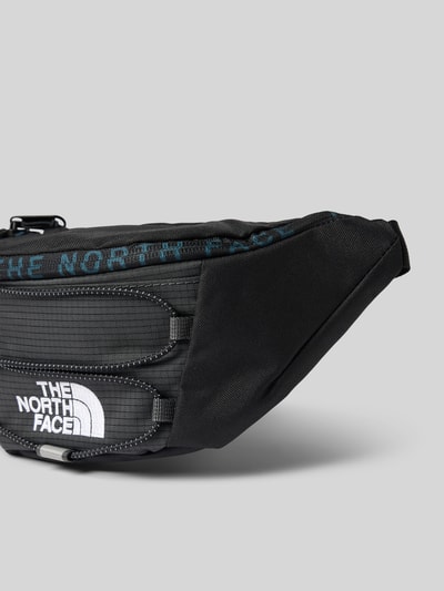Produktfoto, schwarze Bauchtasche mit Logo-Print Modell 'Jester' von The North Face, sichtbare Reißverschlüsse, strukturierte Oberfläche, Kontext: Herren Bauchtasche, Hauptfach, verstellbarer Schulterriemen, Maße 27x16x9 cm, Schulterriemenlänge 30 cm, KI-modifiziertes Bild.