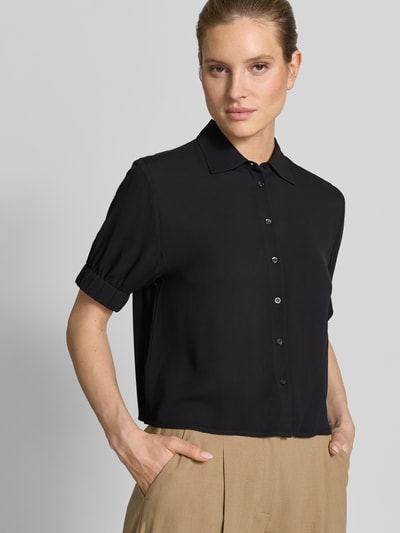 Modelka nosi Regular Fit Bluse aus Viskose mit 1/2-Arm od Emily Van den Bergh, czarna, krój regular fit, kołnierzyk koszulowy, listwa guzikowa, rękaw 1/2, czysta wiskoza, długość tyłu w rozmiarze 36: 54 cm, długość rękawa: 26 cm, ujęcie: z przodu, zbliżenie górnej części ciała.