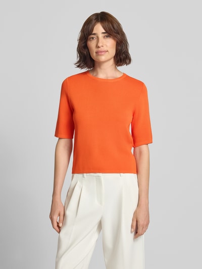Frauenmodel trägt Strickpullover aus Viskose-Mix mit 1/2-Arm von Rich & Royal in Orange, feine Struktur, Regular Fit, gerippter Rundhalsausschnitt, Ganzkörperansicht von vorne.