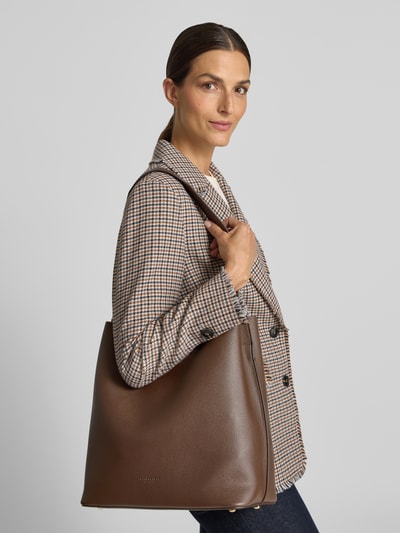 Vrouwenmodel draagt Handtasche in Leder-Optik Modell 'Nelma' van Seidenfelt, bruin, gladde leerlook met logodetail, Ganzkörperansicht van voren. Hoofdvak met magneetsluiting, afneembare schouderband, breedte 31 cm, lengte 35 cm, diepte 17 cm, schouderbandlengte 68 cm.