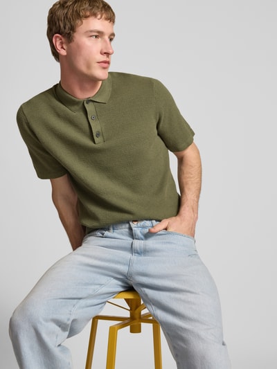 Model męski nosi Regular Fit Poloshirt mit Strukturmuster Modell 'GEORGE' od Jack & Jones, bawełniany miks, guzikowa plisa, kolor oliwkowy, strukturalna tkanina, długość tyłu w rozmiarze M: 67 cm, widok na górną część ciała z przodu.