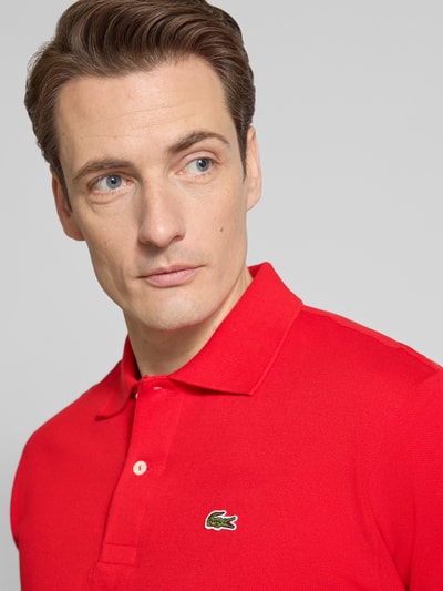 Männermodel trägt Regular Fit Poloshirt aus reiner Baumwolle von Lacoste, efekt: jednolity kolor, krój regular fit, wyhaftowane logo, kołnierzyk polo, rękaw: krótki rękaw, wykończenie: z bocznymi rozcięciami, wykończenie materiału: pika, bawełna, nahaufnahme górnej części ciała.