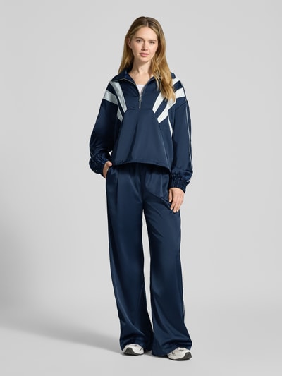 Modelka prezentuje Regular Fit Anorak mit Viskose-Anteil Modell 'Bicca' od Gestuz, granatowy z białymi detalami, krój regular fit, elastyczny materiał z wiskozą, stójka z zamkiem, kieszenie na zamek, elastyczne mankiety, szerokość ramion w rozmiarze 36: 55 cm, szerokość w biuście w rozmiarze 36: 69 cm, długość rękawa w rozmiarze 36: 65 cm, długość pleców w rozmiarze 36: 60 cm, widok całej sylwetki od przodu.