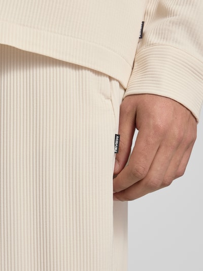 Männermodel trägt Hose mit elastischem Bund in Plissee-Optik von REVIEW, Creme, feine Linienstruktur, Material-Mix mit Stretch-Anteil, Nahaufnahme Oberkörper.