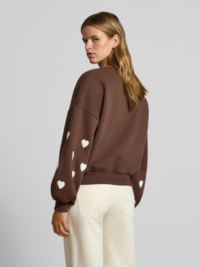 Vrouwenmodel draagt Regular Fit Sweatshirt aus Baumwoll-Mix model 'MACY' van ONLY in bruin met witte hartvormen, Dames sweatshirt, volledige rugaanzicht.