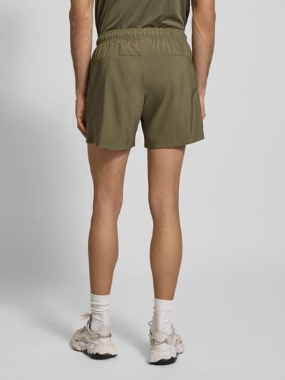 Männermodel trägt Shorts mit elastischem Bund von adidas Training in Oliv, Lockere-Passform, Reißverschlusstaschen, Label-Print, Ganzkörperansicht Rückansicht.