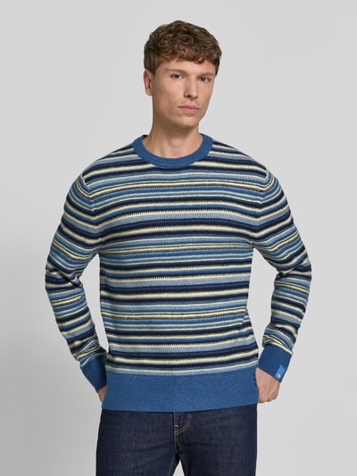 Männermodel trägt Regular Fit Strickpullover mit Streifen-Muster von Scotch & Soda, Blau-Grün-Gelb, Material-Mix mit Woll-Anteil, Nahaufnahme Oberkörper.