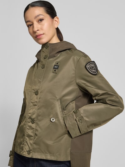 Frauenmodel trägt Regular Fit Jacke mit Logo-Detail Modell 'Marcela' von Blauer Usa in Olivgrün mit Kapuze und Eingrifftaschen, Nahaufnahme Oberkörper. Rückenlänge 60 cm, Schulterbreite 43 cm, Brustweite 47 cm, Ärmellänge 59 cm, Größe S.