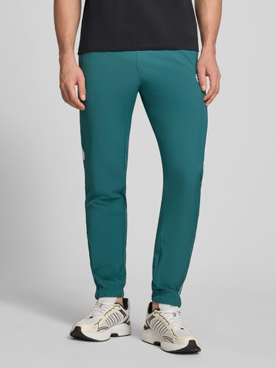Męski model nosi Sweatpants mit Logo-Stitching Modell 'CASPIO' od SERGIO TACCHINI, turkusowy, elastyczny materiał, krój slim fit, logo z przodu, elastyczny pas z troczkiem, kieszenie boczne, elastyczne ściągacze, długość nogawki wewnątrz 78 cm w rozmiarze M, ujęcie całej sylwetki z przodu.