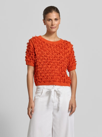 Frauenmodel trägt Strickpullover mit Rundhalsausschnitt und 1/2-Arm von Oui, Reine Baumwolle, Gerader-Schnitt, Gerippter Rundhalsausschnitt, Gerippte-Abschlüsse, orange Farbe, strukturierte Oberfläche, Ganzkörperansicht von vorne.