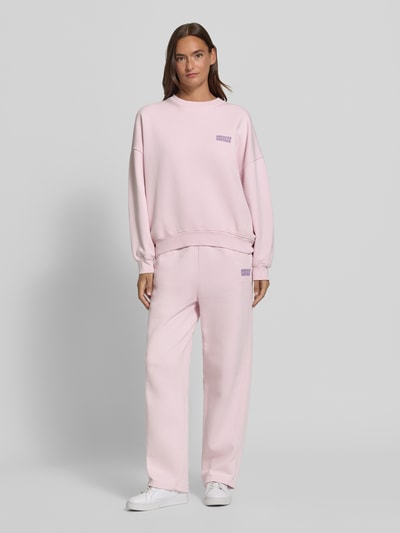Frauenmodel trägt Sweatpants aus reiner Baumwolle mit Logo-Print Modell 'PLIZZY' von American Vintage in Hellrosa, Straight Fit, elastischer Bund, Eingrifftaschen, glatte Textur, Ganzkörperansicht von vorne.