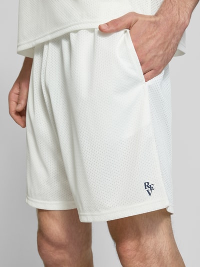Männermodel trägt Shorts aus Mesh mit Logo-Print von REVIEW in Weiß mit seitlichen Eingrifftaschen, Nahaufnahme Oberschenkel. Loose-Fit, elastischer Bund, Bundweite Größe M 42 cm, Innenbeinlänge 18 cm.