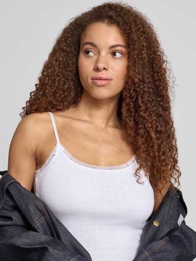 Frauenmodel trägt Slim Fit Top mit Spitzenbesatz von REVIEW in Weiß aus reiner Baumwolle mit Spaghettiträgern und Zierschleifen, Nahaufnahme Oberkörper.