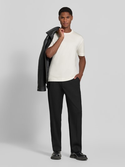 Männermodel trägt T-Shirt mit Logo-Stitching von Emporio Armani in Creme und schwarze Hose, glatte Textur, Ganzkörperansicht von vorne. Elastischer Modal-Mix mit Seide, gerade Passform, Rundhalsausschnitt, Rückenlänge bei Größe M 72 cm.