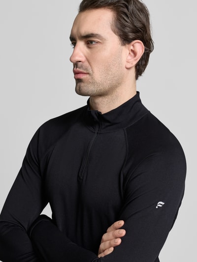 Männermodel trägt Slim Fit Longsleeve mit Logo-Print von Fabletics in Schwarz mit Troyer-Kragen und Kinnschutz, Nahaufnahme Oberkörper.