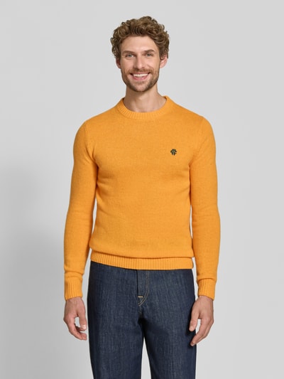 Männermodel trägt Slim Fit Strickpullover aus reiner Wolle mit Label-Stitching von MCNEAL in Orange, gerippte Abschlüsse, Ganzkörperansicht von vorne.