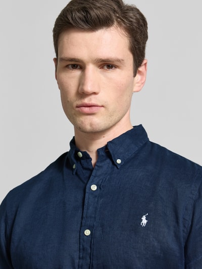 Męski model nosi Slim Fit Freizeithemd aus reinem Leinen od Polo Ralph Lauren w jednolitym granatowym kolorze, bliska perspektywa górnej części ciała.
