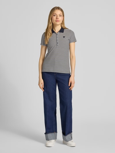 Kobiece model nosi Regular Fit Poloshirt aus Baumwoll-Mix od Tom Tailor, efekt: wzór w paski na całej powierzchni, wyhaftowany motyw, kołnierzyk polo, dekolt w serek, krótki rękaw, wykończenie materiału: pika, materiał: mieszanka bawełny, widok całej sylwetki z przodu.