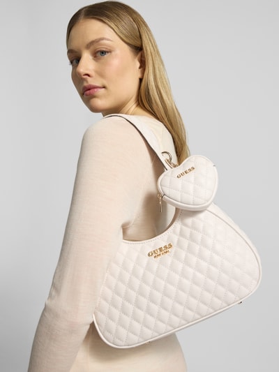 Frauenmodel trägt Handtasche mit Steppnähten Modell 'ATABEY HOBO' von Guess, Farbe Creme, Label-Applikation, Anhänger, Hauptfach mit Reißverschluss, Tragehenkel, Schulterriemen 50 cm, Breite 22 cm, Länge 20 cm, Tiefe 8 cm, Ganzkörperansicht Rückansicht.