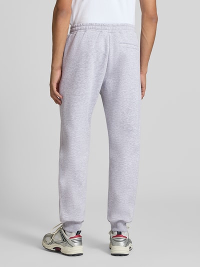 Mężczyznamodel nosi Slim Fit Sweatpants mit Tunnelzug od REVIEW w jasnoszarym kolorze, wpuszczane kieszenie, kieszeń z tyłu, długość wewnętrzna nogawki w rozmiarze M: 80 cm, widok całej sylwetki z tyłu.