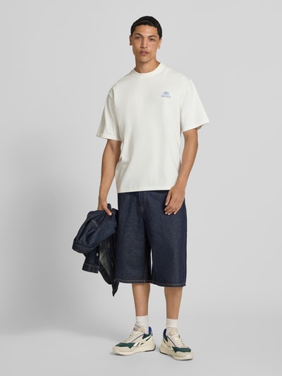 Männermodel trägt Herren T-Shirt mit Statement-Print und Rundhalsausschnitt von Redefined Rebel, Baumwoll-Mix, Relaxed-Fit, Modell 'Bruno', Rückenlänge bei Größe M 70 cm, helle Grundfarbe mit dunkler Jeans und Sneakers, Ganzkörperansicht von vorne.