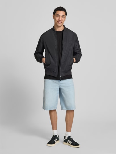 Männermodel trägt T-Shirt aus Baumwolle mit Rundhalsausschnitt von G-Star Raw, schwarz, Regular Fit, Kombi mit Shorts, Ganzkörperansicht von vorne.