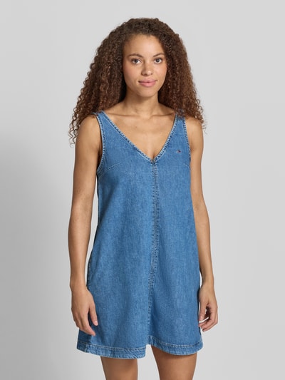 Frauenmodel trägt Ausgestelltes Jeanskleid aus reiner Baumwolle von Tommy Jeans in Denim-Optik, Mini-Länge, V-Ausschnitt, Label-Patch, Label-Stitching, schmale Träger, ohne Ärmel, seitliche Eingrifftaschen, Twill-Materialverarbeitung, reine Baumwolle, Ganzkörperansicht von vorne.